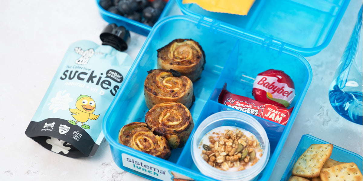 Close-up of sausage tortilla pinwheels made with grated carrot and courgette served in a lunchbox with various snacks 