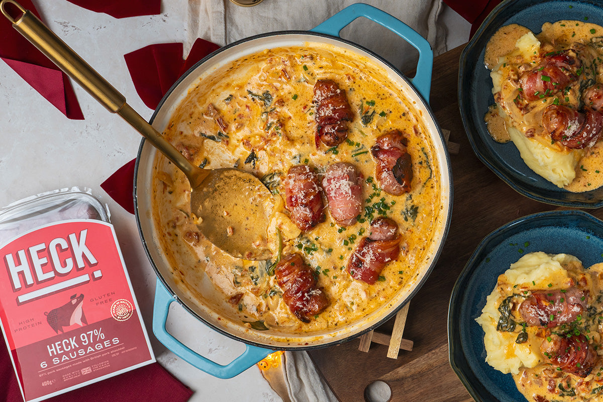 Crispy bacon-wrapped pork sausages served in a creamy Parmesan and sun-dried tomato sauce, garnished with chives and spinach.